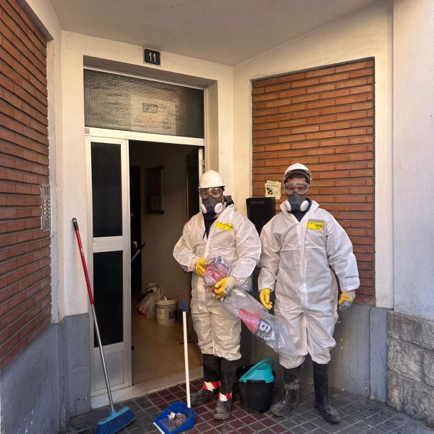 Dos profesionales con trajes blancos y mascarillas en la puerta de un edificio 