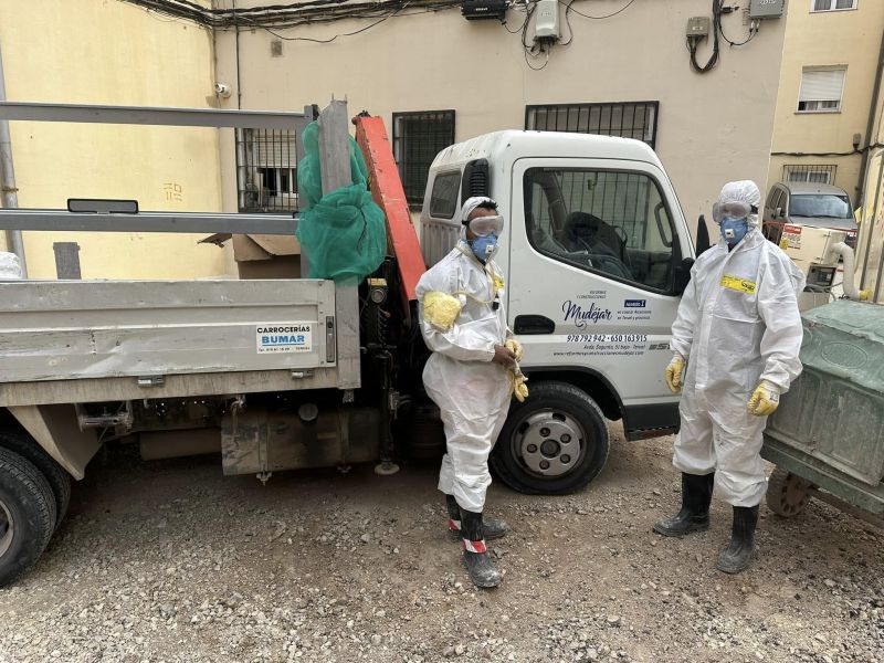 Imagen de dos trabajadores con traje blanco profesional y mascarilla delante de grúa 
