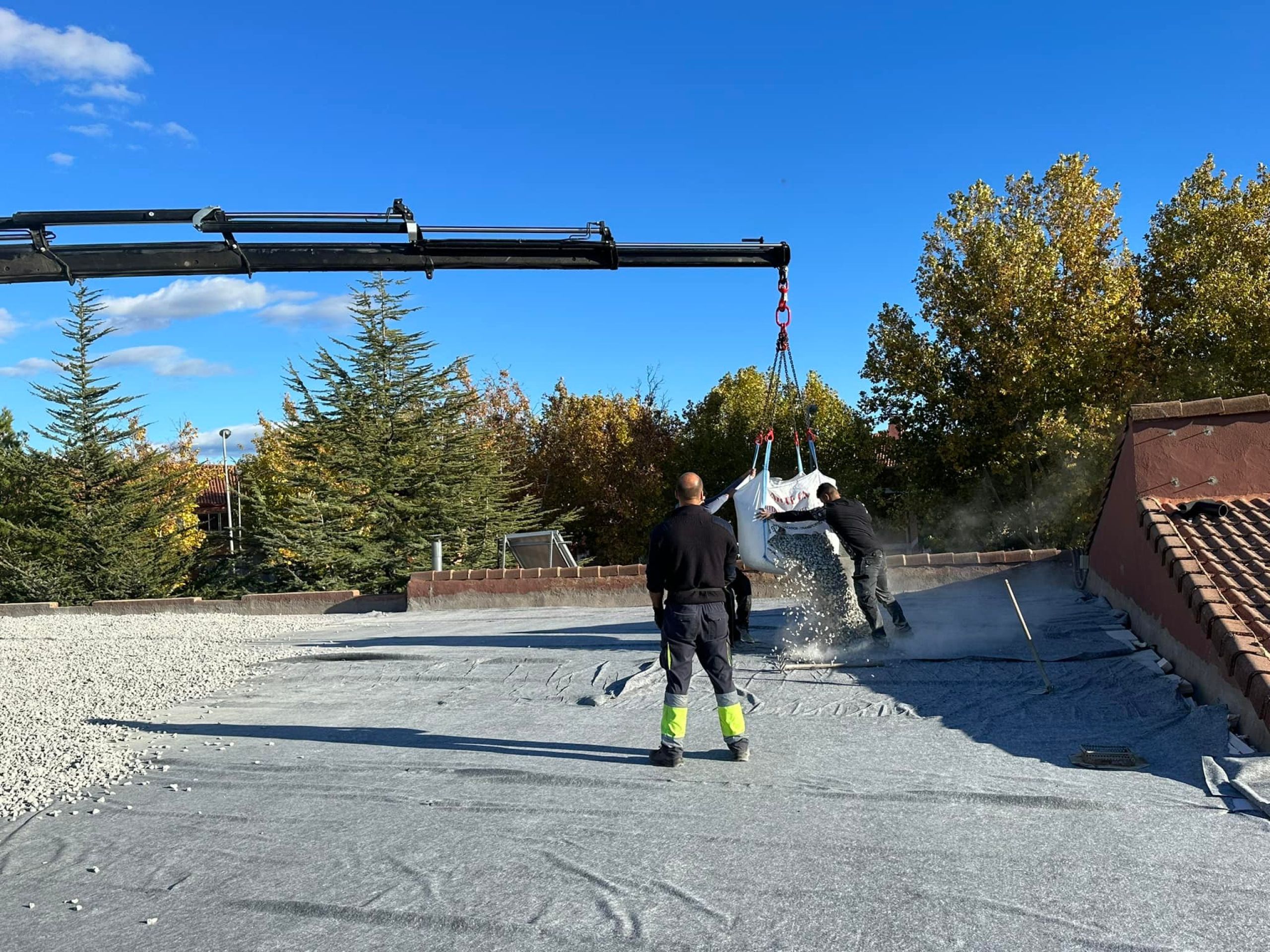 Trabajadores descargando grava en una azotea con grúa durante una obra de construcción.