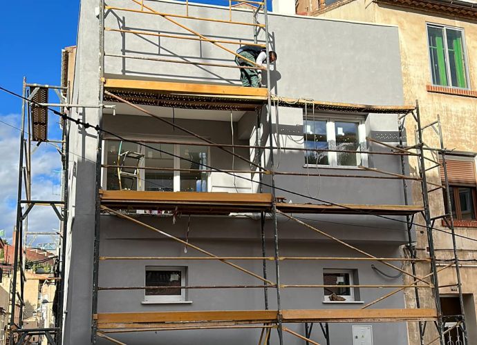 Obrero sobre andamio reformando fachada de color gris 