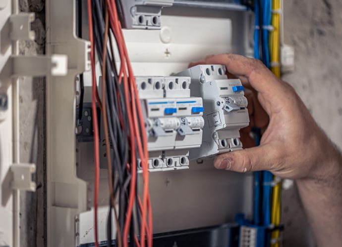 Técnico manipulando interruptores en un cuadro eléctrico con cables visibles.