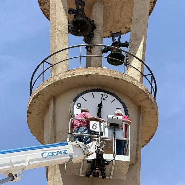 Dos trabajadores subidos en una grúa a lo alto de una torre con reloj 