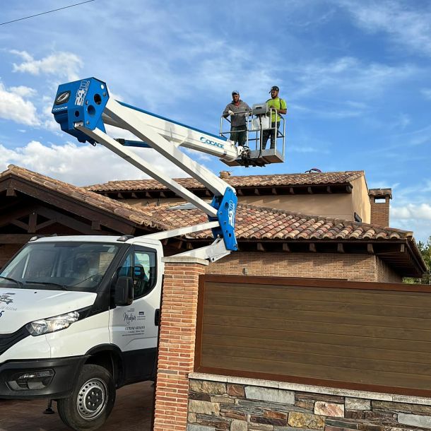 Dos profesionales subido a una grúa por encima del tejado de un chalet 