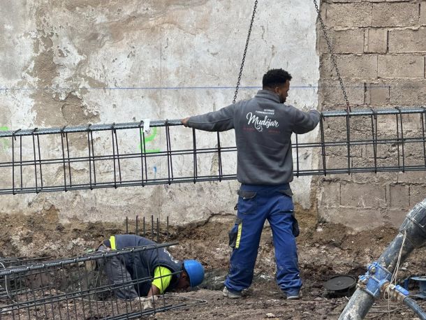 Obrero con sudadera de construcciones mudéjar sujetando base de grúa con las manos 